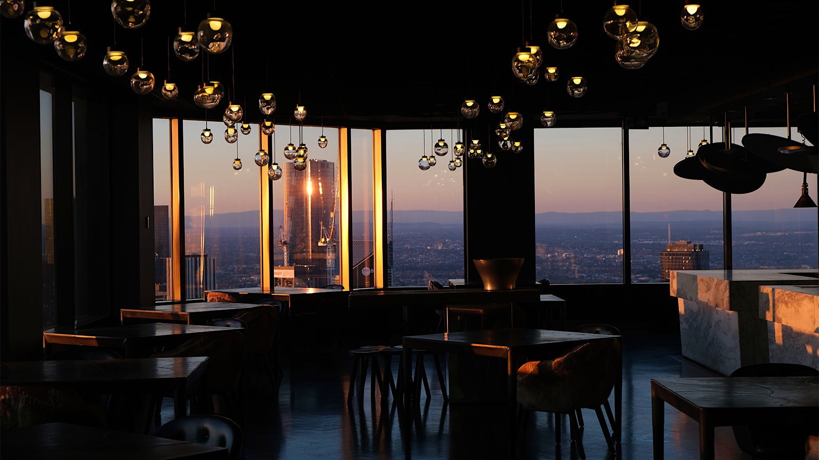 Black tables at Vue de Monde, where the dining room has a herringbone parquet floor, leather seats, spherical glass lighting fixtures and views of Melbourne